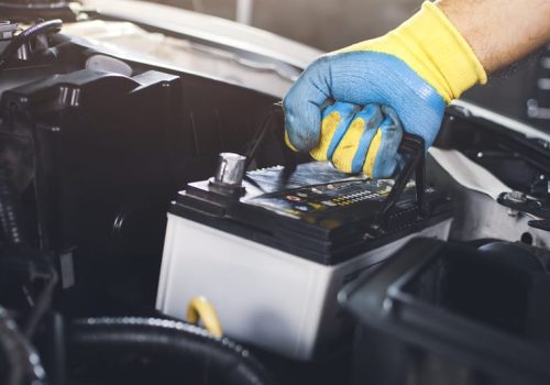 Car-mechanic-replacing-the-old-car-battery-with-a-brand-new-one-wearing-gloves-and-pulling-out-the-battery-installing-a-brand-new-one